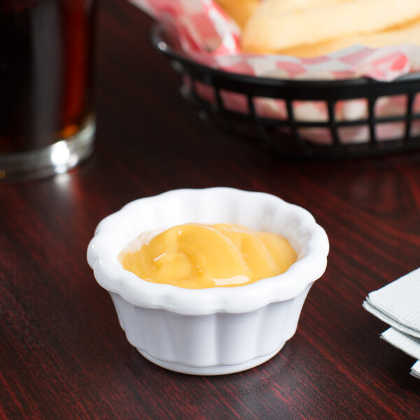 A white Carlisle ramekin filled with yellow sauce on a table.