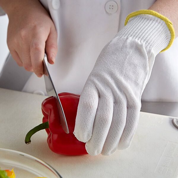 A person wearing MercerGuard white gloves cutting a red pepper.