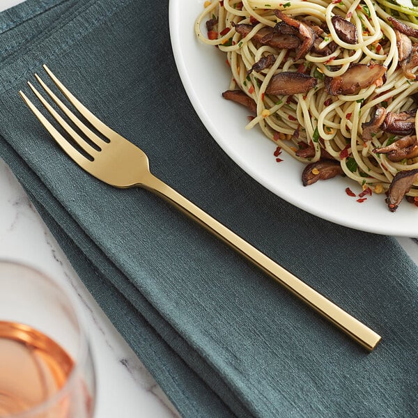 An Acopa Phoenix stainless steel dinner fork next to a plate of spaghetti and mushrooms.