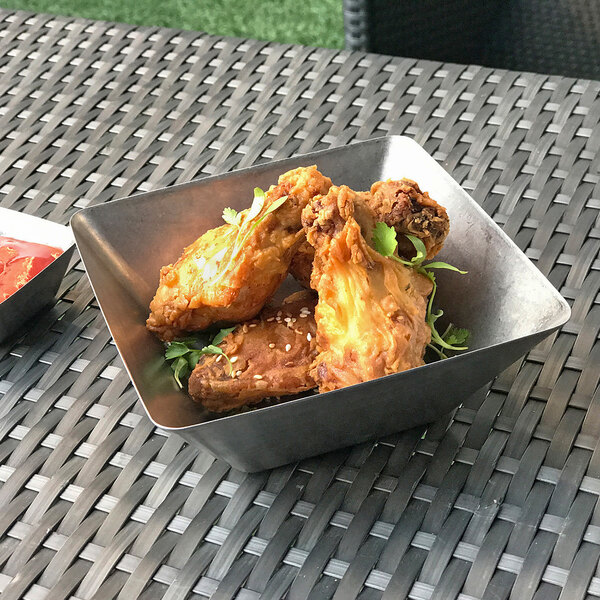 A metal bowl of fried chicken with sauce on a table.