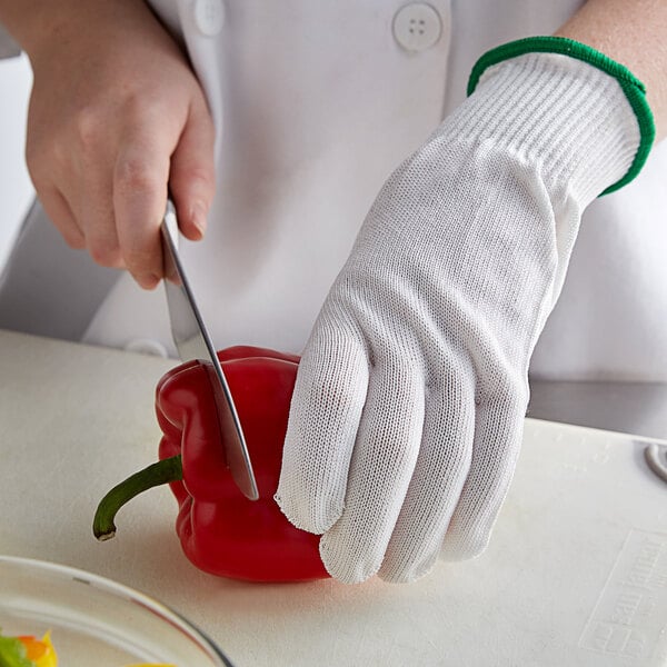 A person wearing white Mercer Culinary cut-resistant gloves cutting a red pepper.
