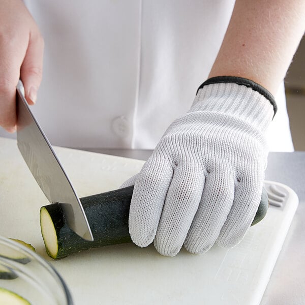 A person cutting a cucumber with a Mercer Culinary white cut-resistant glove.