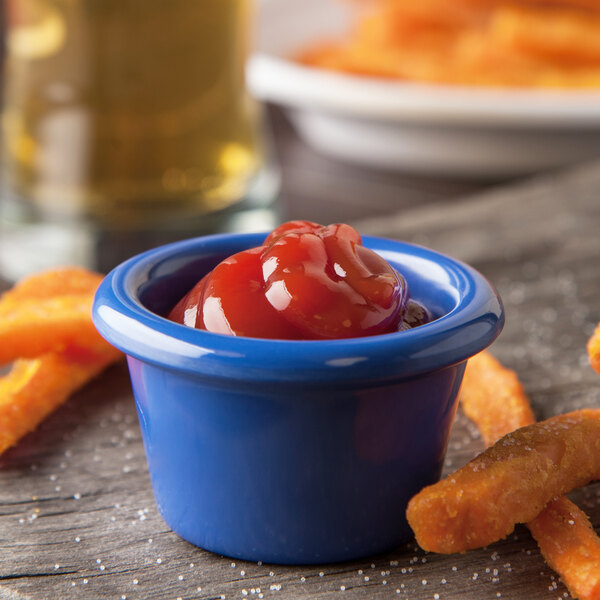 A blue Carlisle ramekin filled with ketchup next to french fries on a wood table.