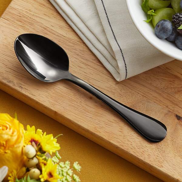 An Acopa Vernon stainless steel teaspoon on a table with a bowl of fruit.