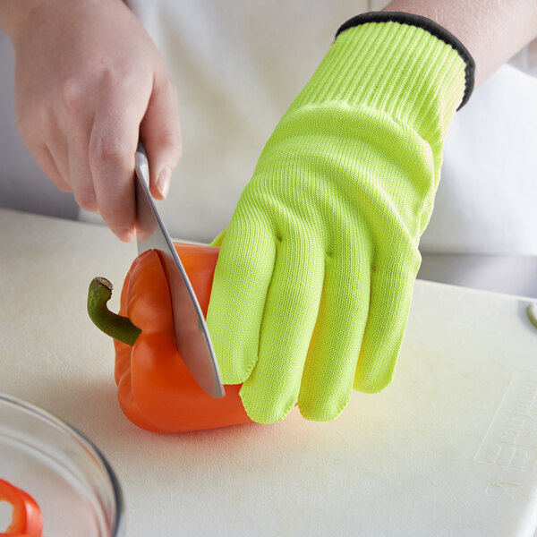 A person wearing yellow Mercer Culinary cut-resistant gloves cutting a bell pepper on a counter.