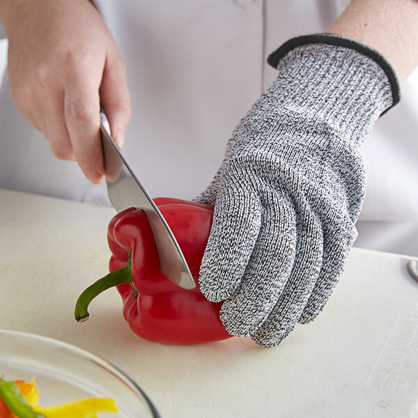 A person wearing a MercerMax cut-resistant glove cuts a red pepper on a counter.
