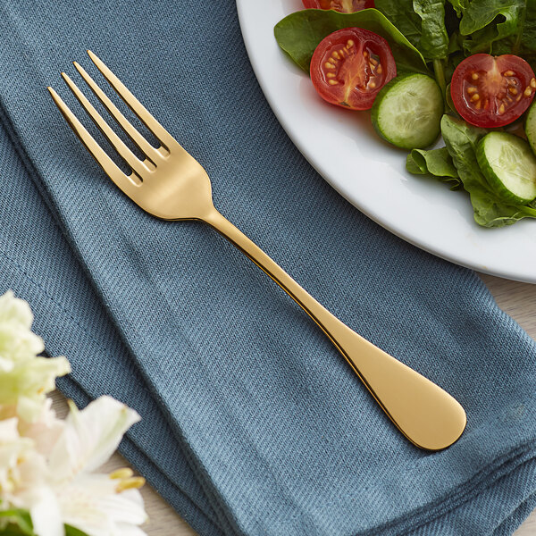 An Acopa Vernon gold heavy weight stainless steel salad fork on a plate of salad.