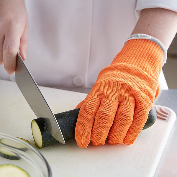 A person cutting a cucumber with a knife while wearing an orange Mercer Culinary Millennia Level A4 Cut-Resistant Glove.