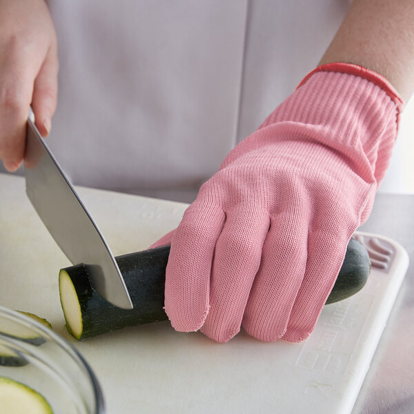 A person using a Mercer Culinary pink cut-resistant glove to cut a zucchini on a counter.