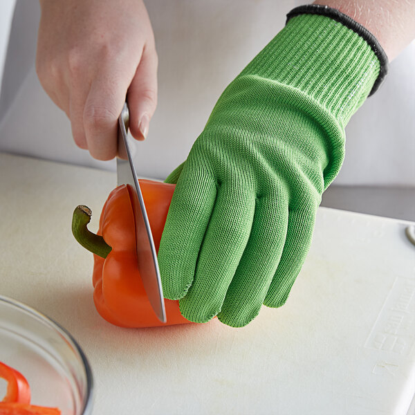 A person wearing green Mercer Culinary cut-resistant gloves cutting a bell pepper.