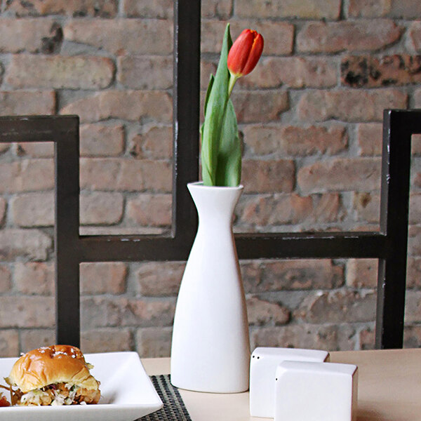 A red tulip in a white Front of the House Kyoto bud vase on a table.