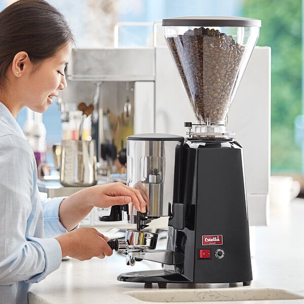 A woman using an Estella Caffe espresso grinder on a counter in a professional kitchen.
