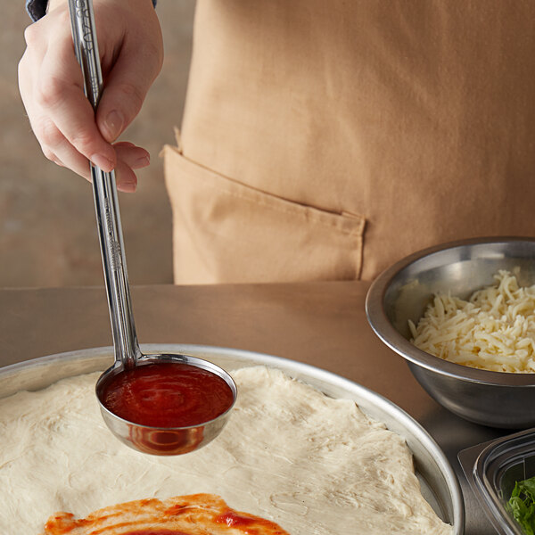 A person using a Vollrath stainless steel ladle to put red sauce on a pizza.