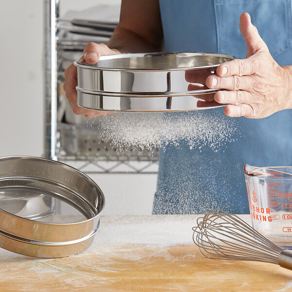 A person sifting flour into a Matfer Bourgeat stainless steel sieve.