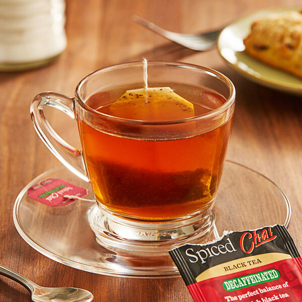 A glass cup of Bigelow Spiced Chai decaffeinated tea with a tea bag on a saucer.
