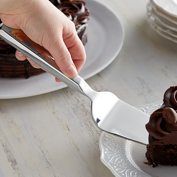 A hand using Vollrath stainless steel pastry server to slice a chocolate cake.