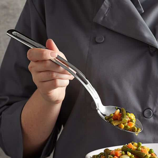 A woman using a Vollrath stainless steel slotted serving spoon to serve food.