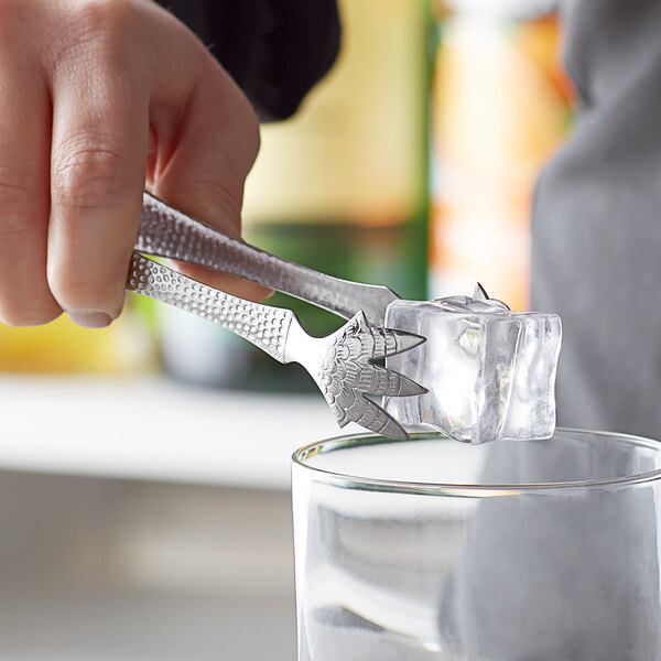 A person using Vollrath stainless steel ice tongs to add ice to a glass.