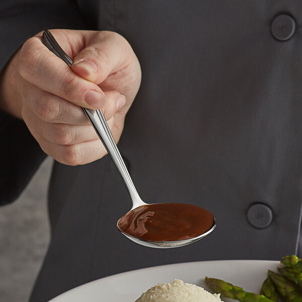 A person using a Vollrath stainless steel ladle to serve sauce on a plate.