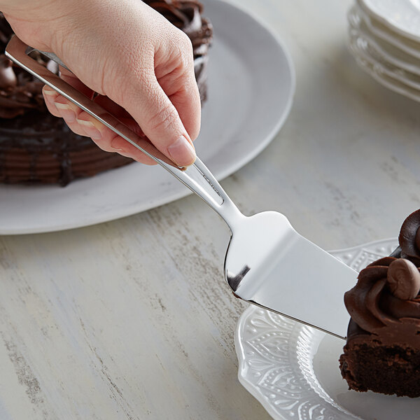 A person cutting a chocolate cake with a Vollrath stainless steel pastry server.