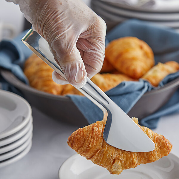 A person using Vollrath silverplated stainless steel pastry tongs to serve a croissant.