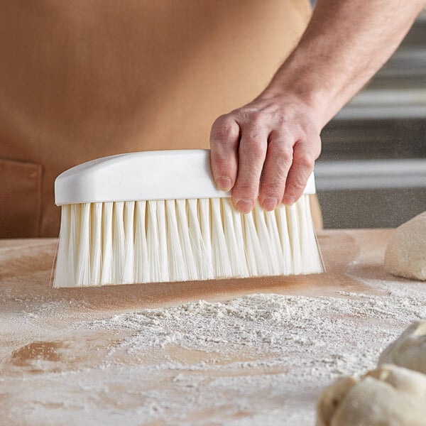 A person using an Ateco white nylon bristle bench brush to clean dough.