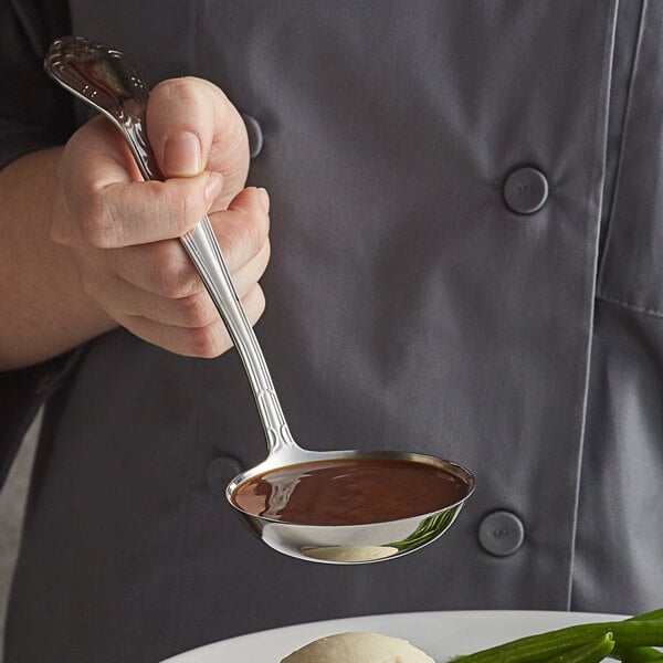 A person using a Vollrath stainless steel ladle to serve brown liquid.