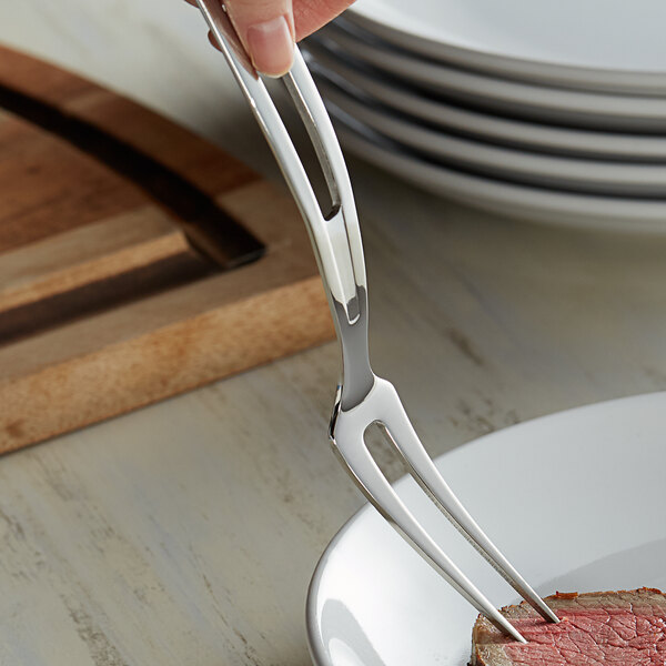 A person using a Vollrath stainless steel serving fork to serve meat on a plate.
