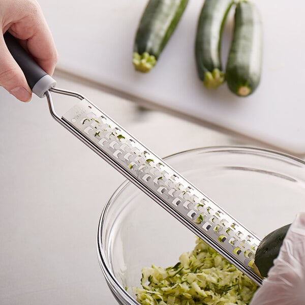 A hand grating cucumbers with a MercerGrates extra coarse grater into a bowl of food.