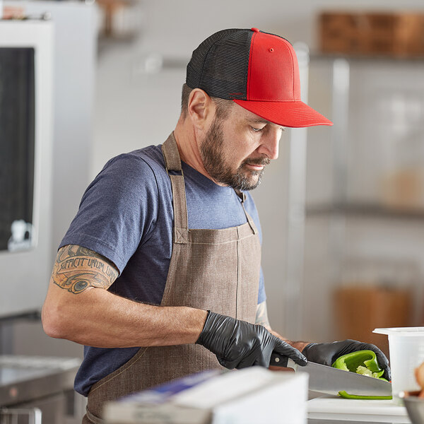 A man in a red Mercer Culinary trucker cap and apron cutting vegetables.