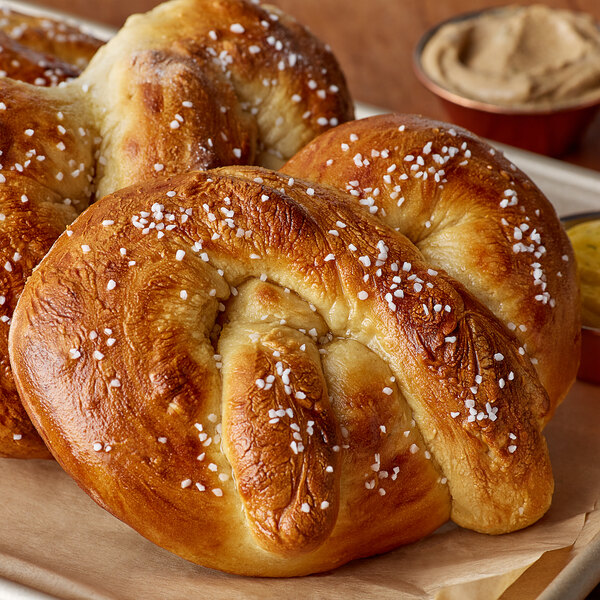 A close up of two soft pretzels on a tray with mustard and butter.