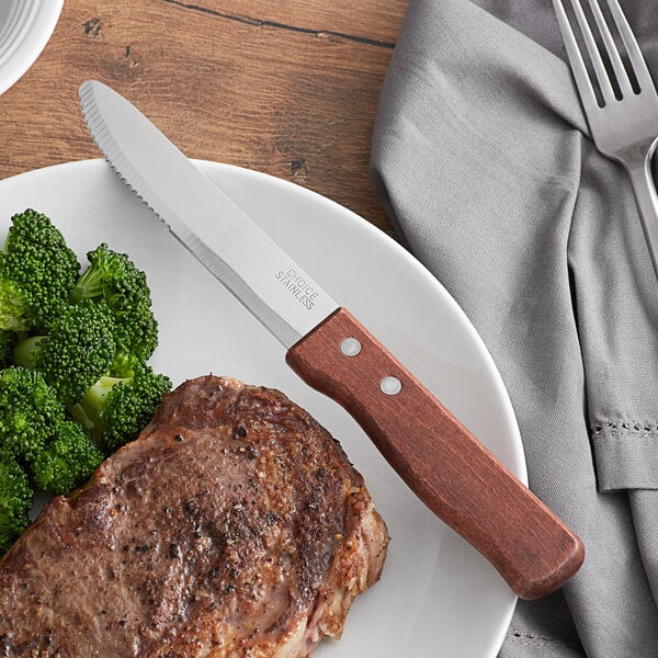 A plate of food with a steak and broccoli with a Choice jumbo steak knife on the table.