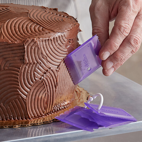 A person using a purple plastic Wilton cake comb to decorate a cake.