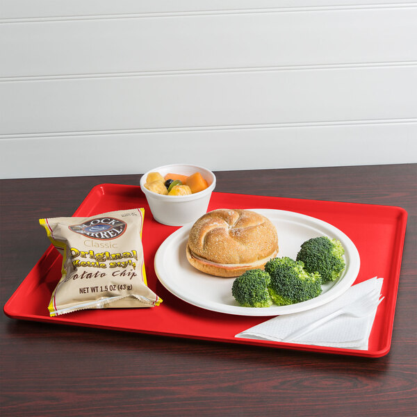 A red Cambro dietary tray with a sandwich, chips, and a drink on it.