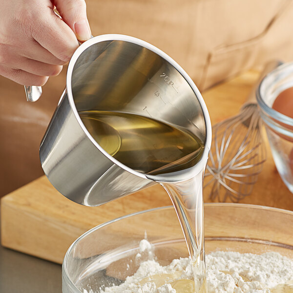 A person using a Linden Sweden stainless steel measuring cup to pour liquid into a bowl of flour.
