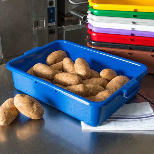 A blue Carlisle bus tub with potatoes in it on a counter.
