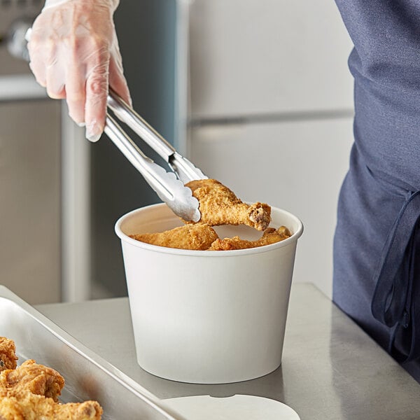 A person using tongs to put fried chicken in a Choice white food bucket.