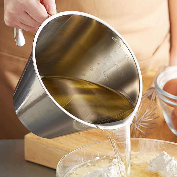 A person using a Linden Sweden stainless steel measuring cup to pour liquid into a bowl.