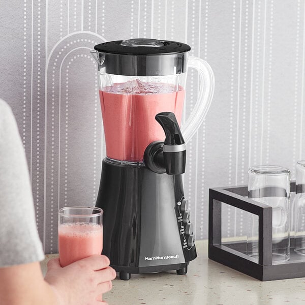 A woman using a Hamilton Beach Wave Station blender to make a glass of pink liquid.