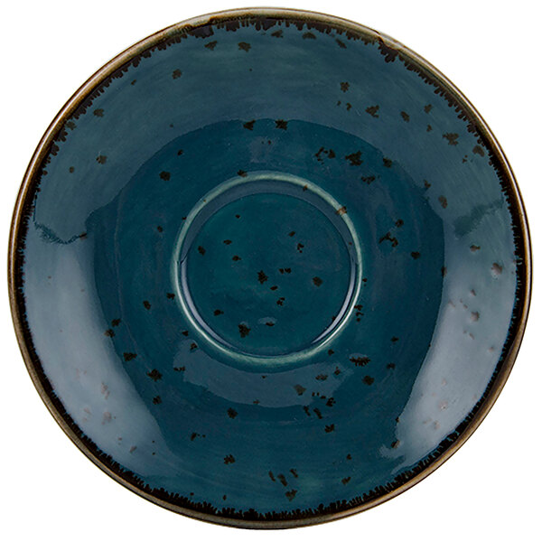 A Tuxton TuxTrendz Artisan Geode Azure saucer with a blue plate and black specks on a table.