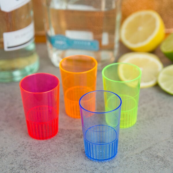 A group of Fineline Quenchers mixed neon plastic shooter glasses on a table with lime slices.