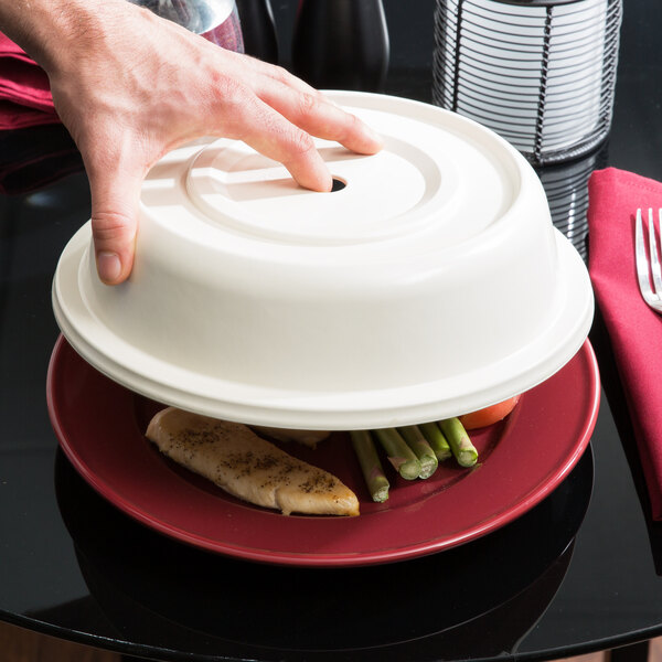A person's hand using a Carlisle bone plate cover to lift a plate of food.