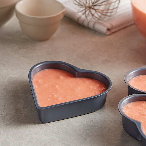 A Fox Run mini heart shaped cake pan with pink liquid inside.