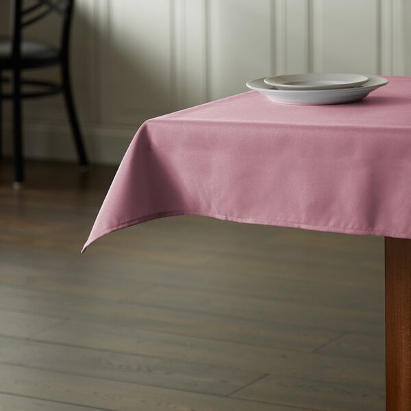 A square pink Intedge polyester table cover on a table with plates.