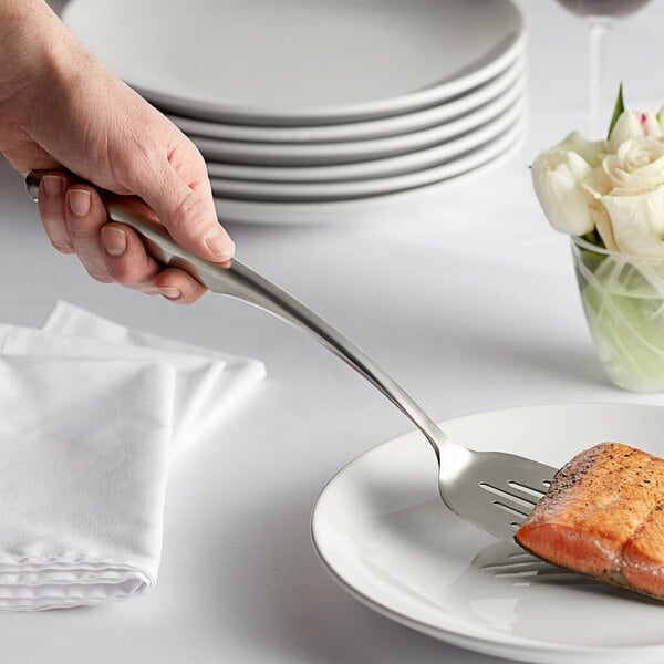 A person using a Tablecraft Dalton stainless steel slotted turner to serve a piece of salmon on a plate.