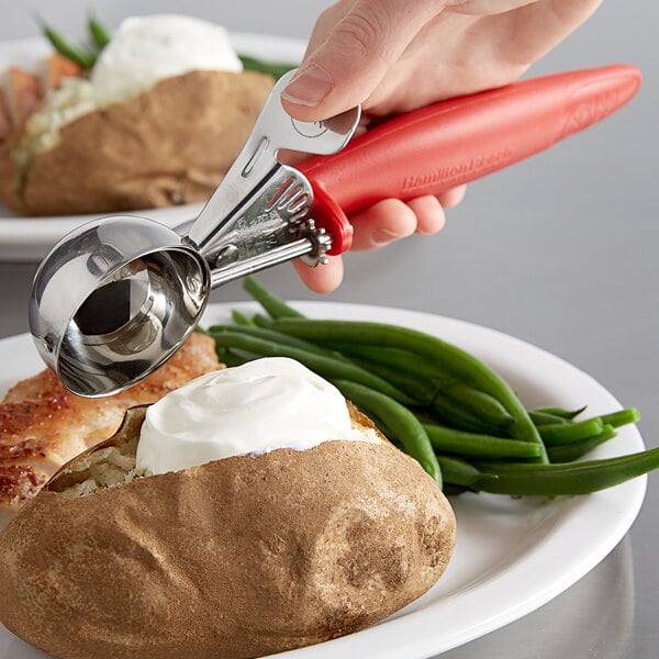 A hand using a red Hamilton Beach ice cream scoop to scoop potatoes.