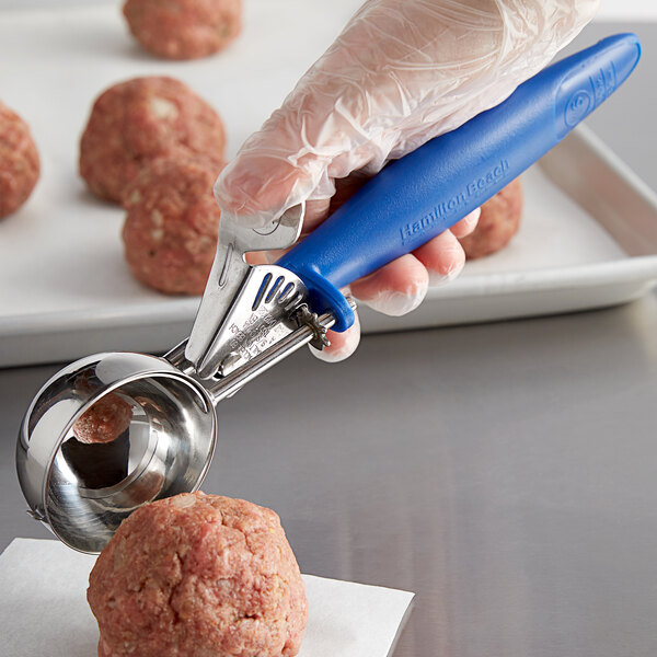 A person using a Hamilton Beach blue handled metal scoop to make meatballs.
