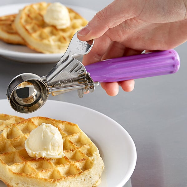 A hand using a purple Hamilton Beach #40 orchid thumb press scooper to scoop ice cream onto a waffle.