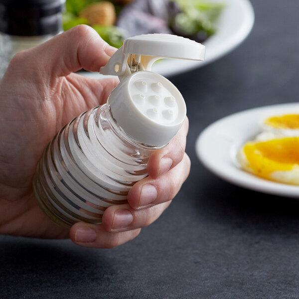A hand holding a Tablecraft beehive shaker with a white cap filled with salt.