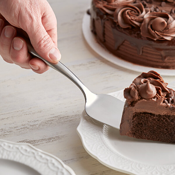 A hand using a Tablecraft Dalton stainless steel cake server to cut a piece of chocolate cake.